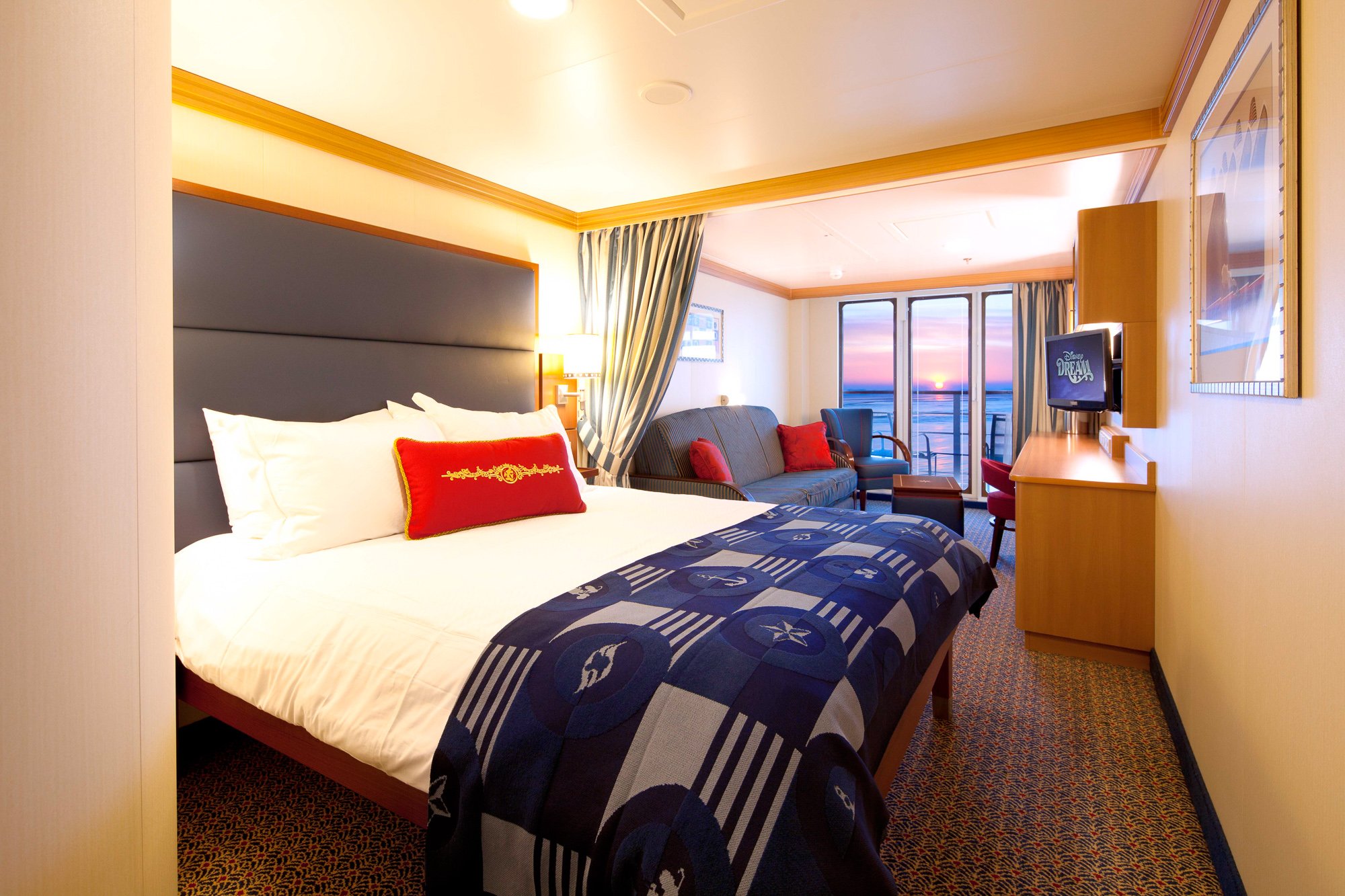 The parents' bed in the foreground of the Deluxe Family Oceanview Stateroom with Verandah on Disney Dream, with curtain to separate from the convertible kids' sleeping area